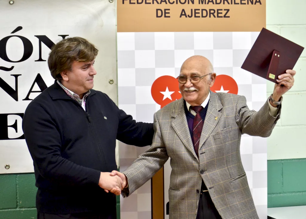 Manolo Guerra levanta orgulloso su placa, que le acaba de entregar el presidente de la Federación Madrileña, Agustín García Horcajo. Foto: FMB / Damas y Reyes