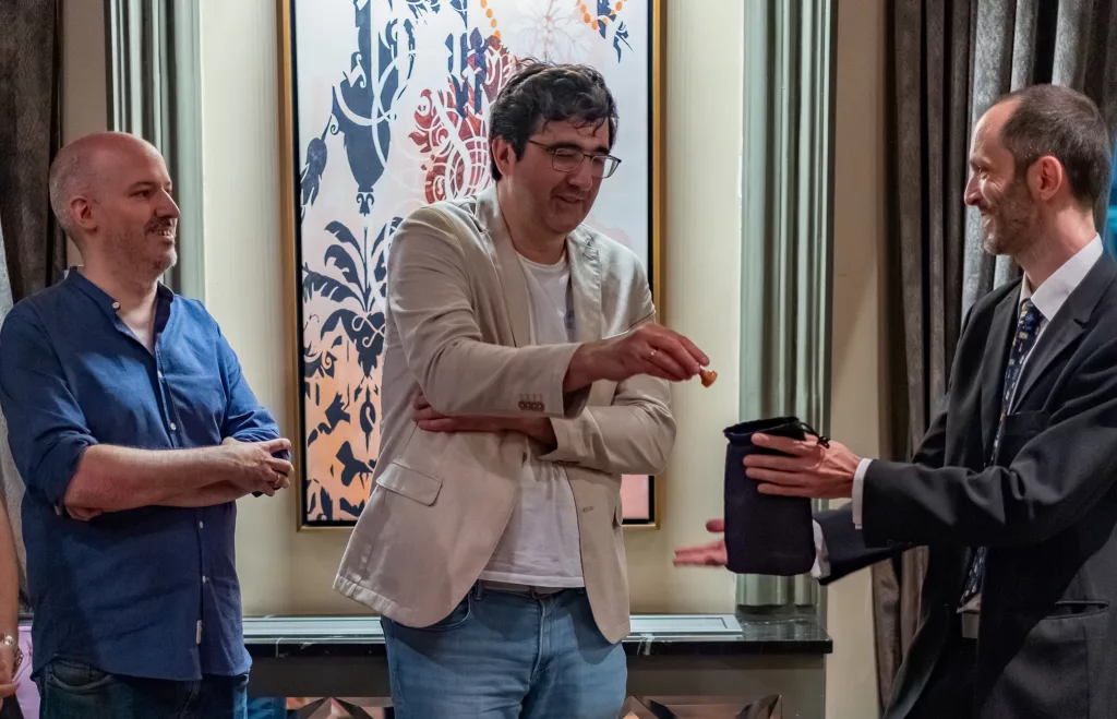 Kramnik, en el sorteo de colores previo al duelo, saca un peón blanco de la bolsa que sostiene el árbitro, Daniel Rodríguez. A su izquierda, David Martínez. Foto: FMB / Damas y Reyes