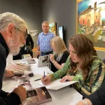 Juan Campos, con Judit Polgar, firmando su libro. A su lado están sus hermanas, Susan y Sofia, a la que podemos ver de refilón. Foto cedida por Juan Campos